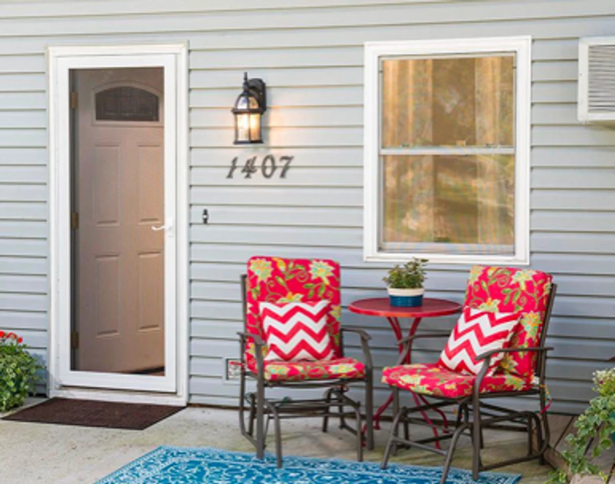 Exterior view: white screen door next to two red-cushion outdoor chairs.